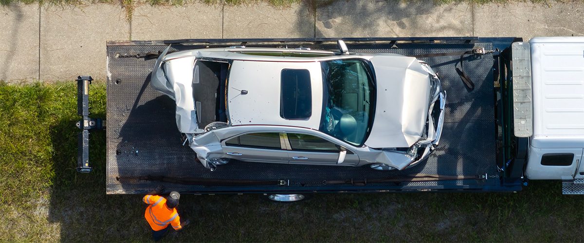 Driver loading wrecked vehicle into flatbed tow truck in Johnson County, KS.